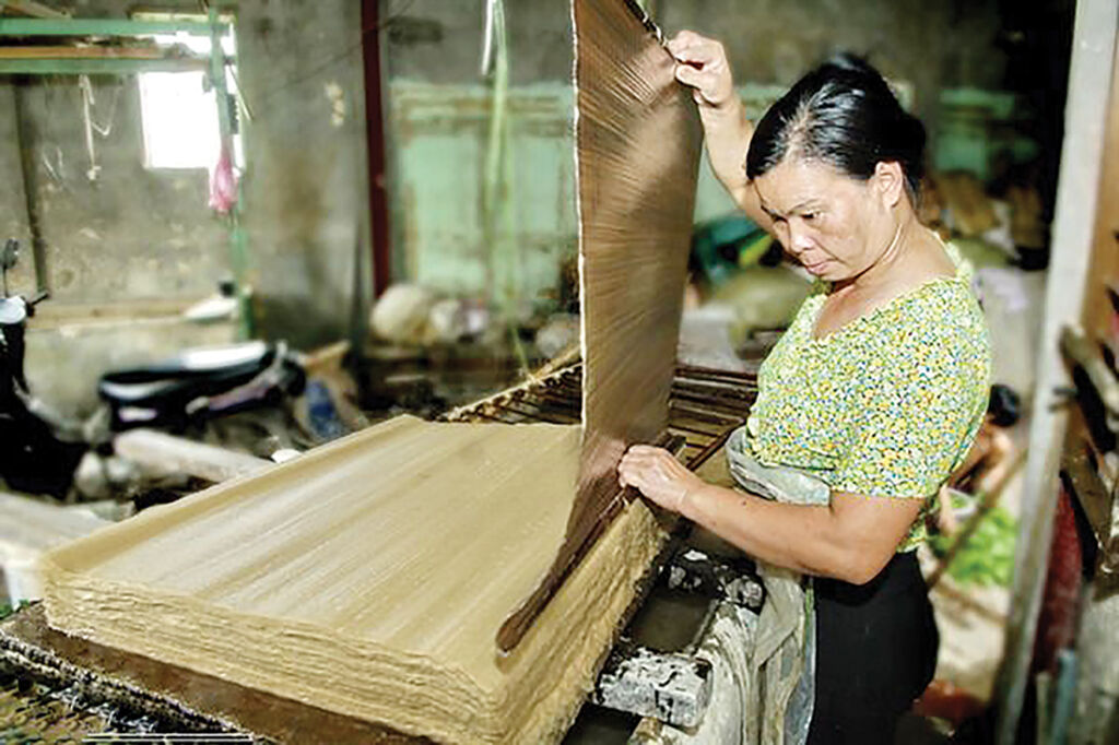 A woman lifting a wet sheet of Dó paper from a stack
